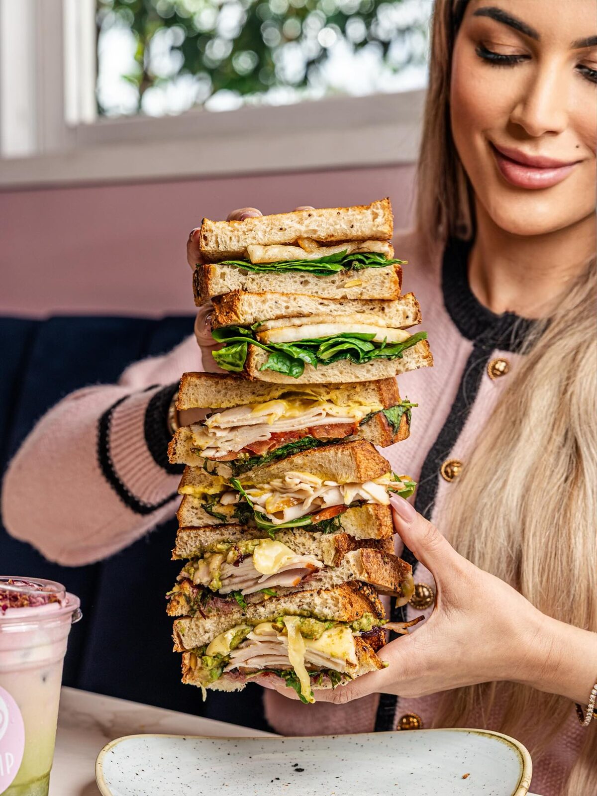 A towering toasted club sandwich stack with chicken, bacon, egg, cheese and greens held up at Soft Sip