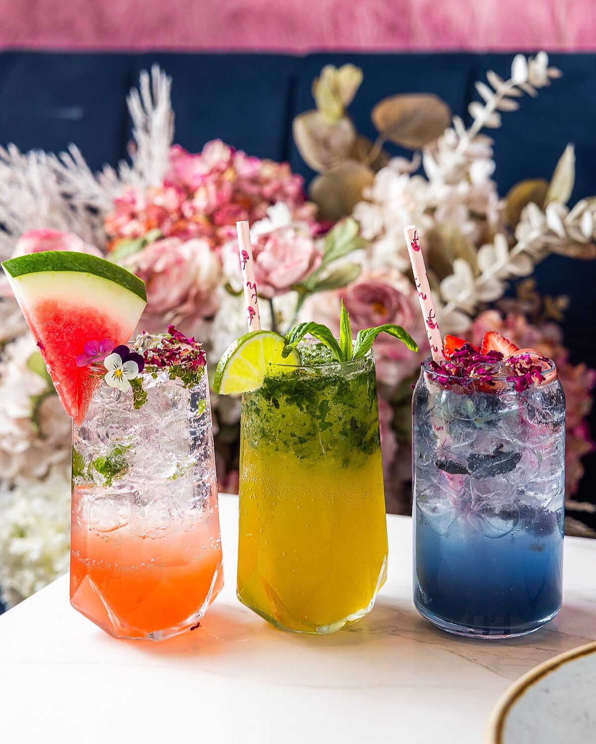 Watermelon, minted lemonade and blue butterfly pea mocktails in front of pink flowers