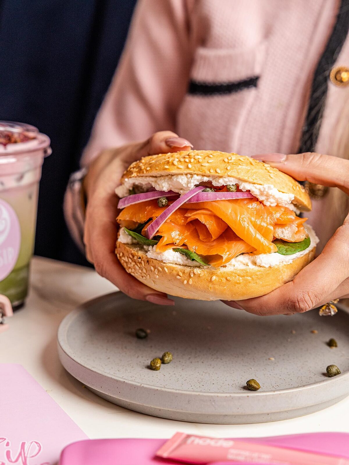 Smoked salmon bagel with cream cheese, red onion, capers and rocket held in two hands