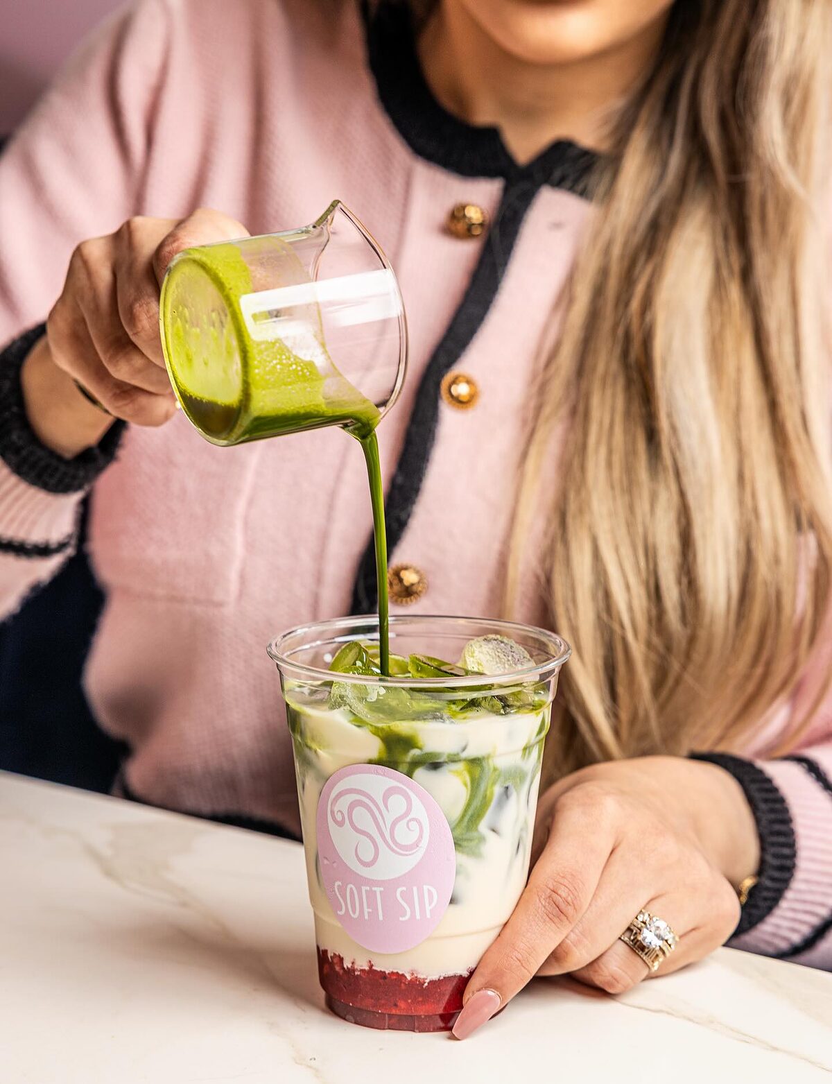 Matcha being poured over milk and strawberry in a Soft Sip cup